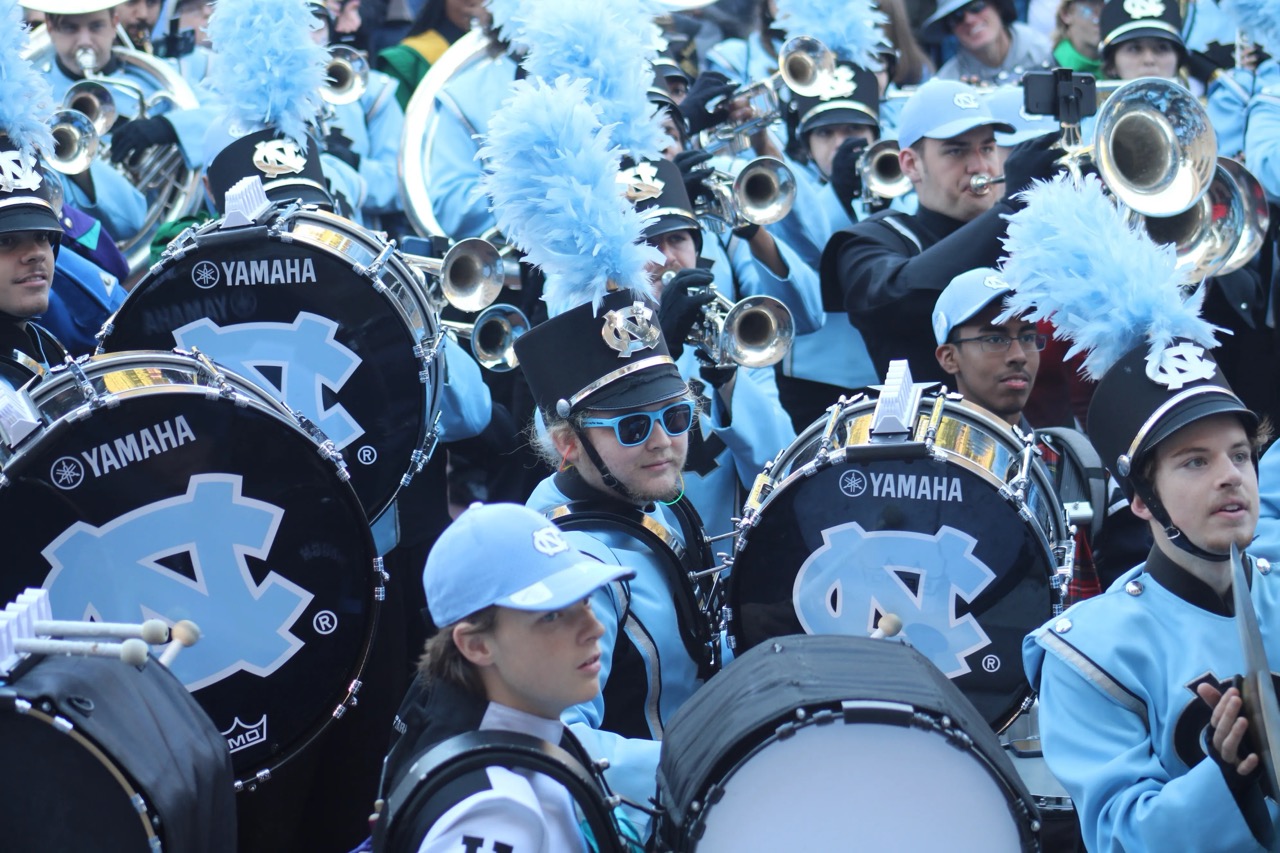 Picture of band members at a football game holding bass drums and other percussive equipment